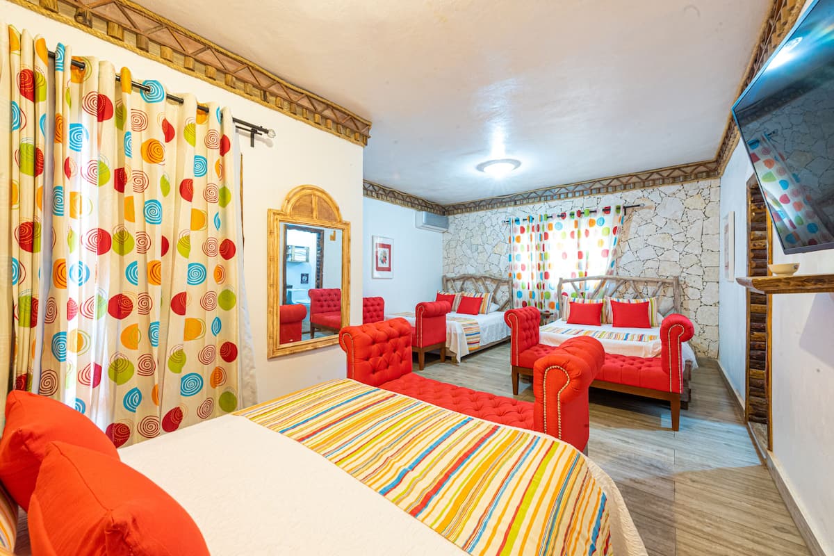 A hotel room with a bed, two red armchairs, a sofa, a mirror, and a television.