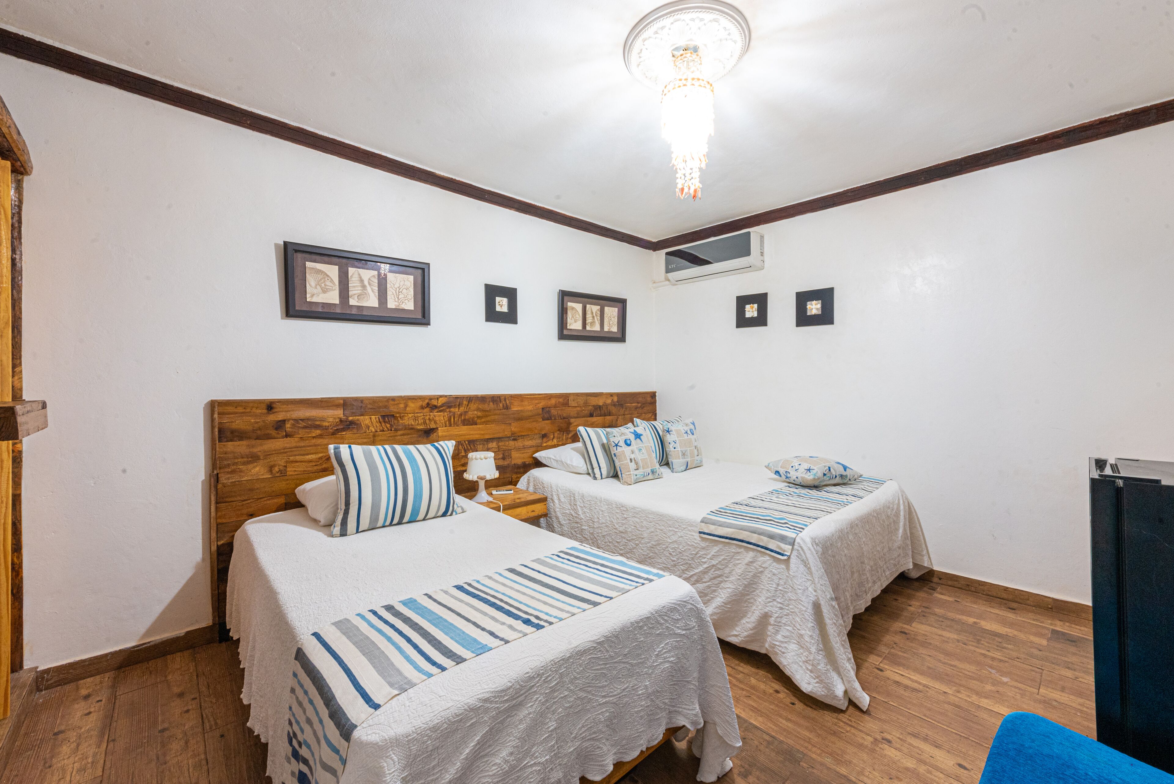 Een hotelkamer met twee bedden, houten hoofdeinden, wit beddengoed en een kroonluchter.