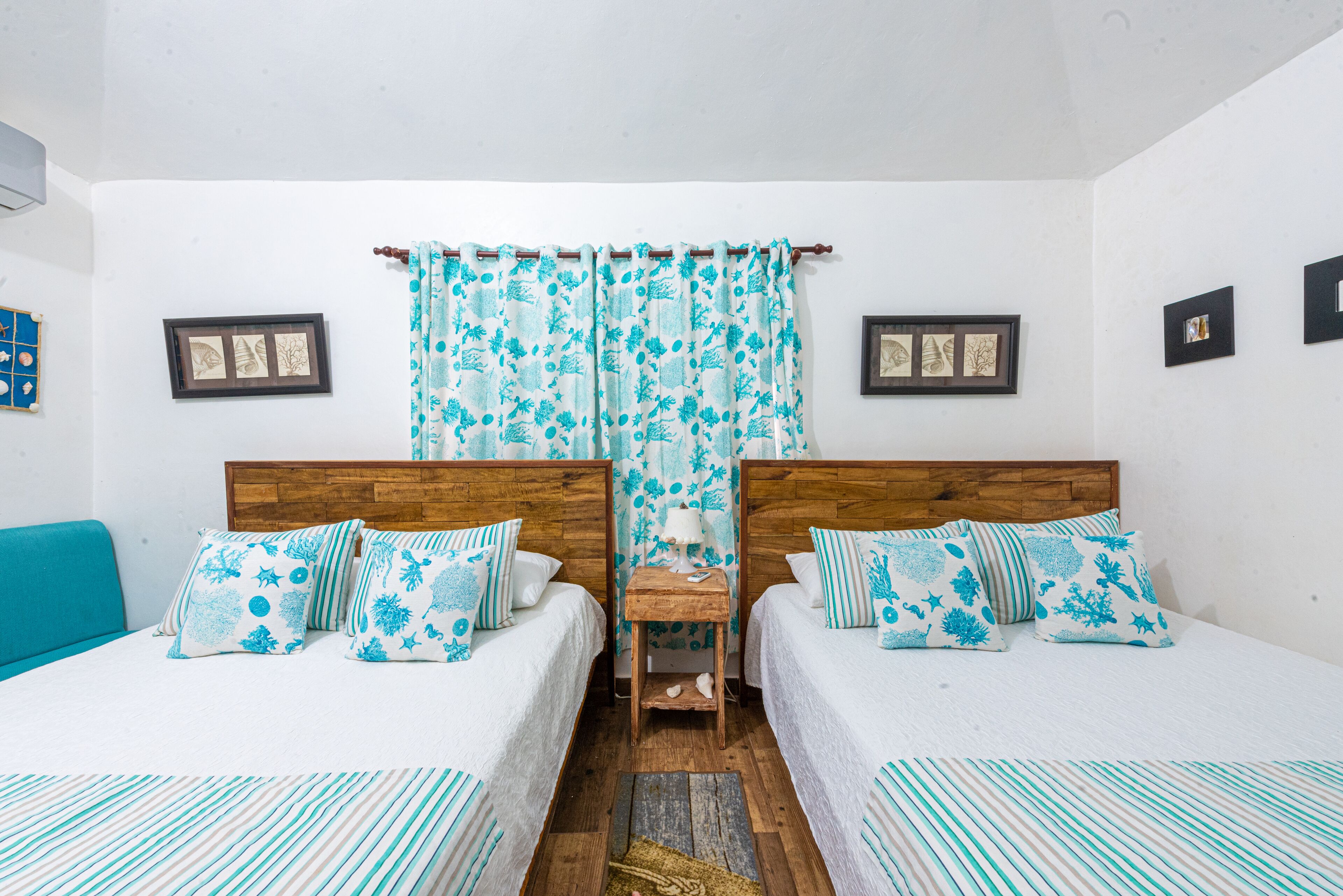 A double room with two beds, a wooden headboard, a small table with a lamp, and a curtain with a leaf pattern.