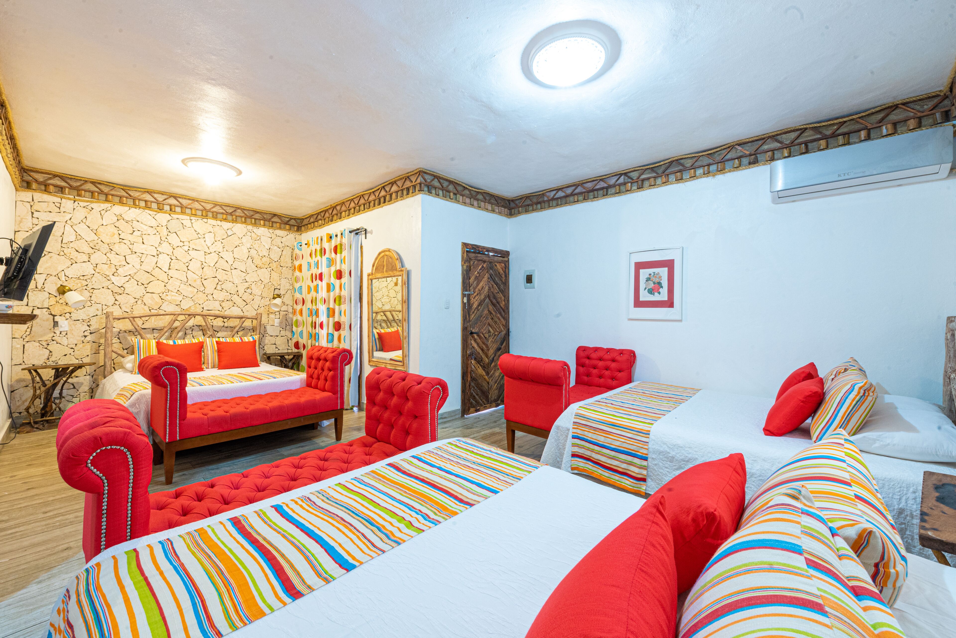 A hotel room with two beds, a red sofa, a wooden chair, and a stone wall.