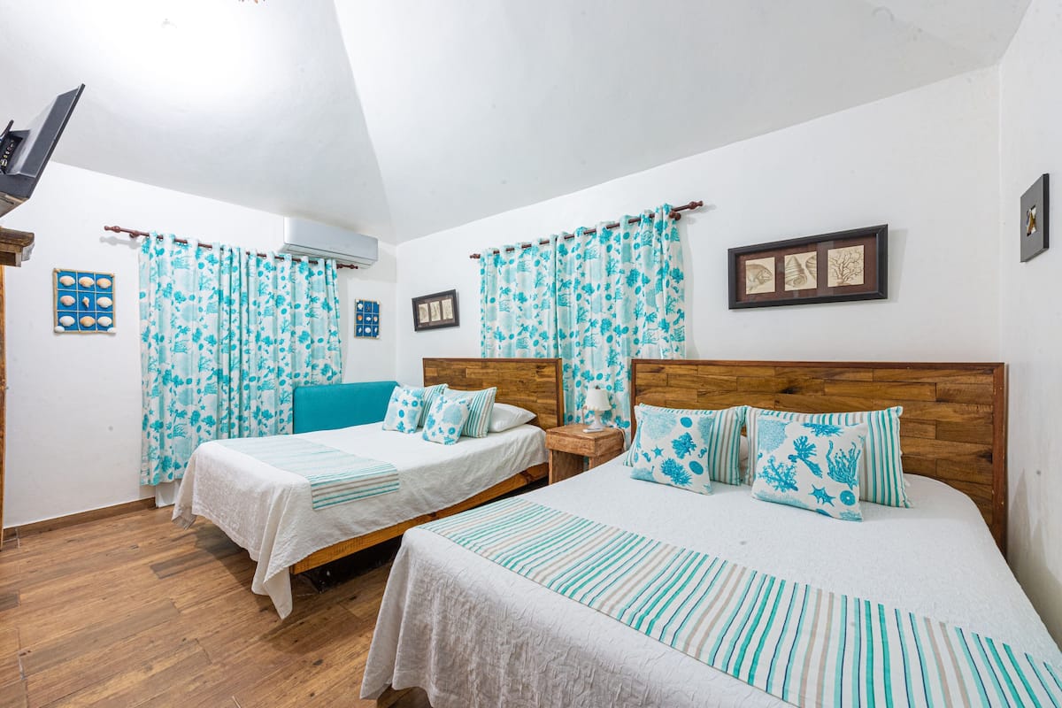 A room with two beds, wooden headboards, a small table, and a wall-mounted air conditioner.