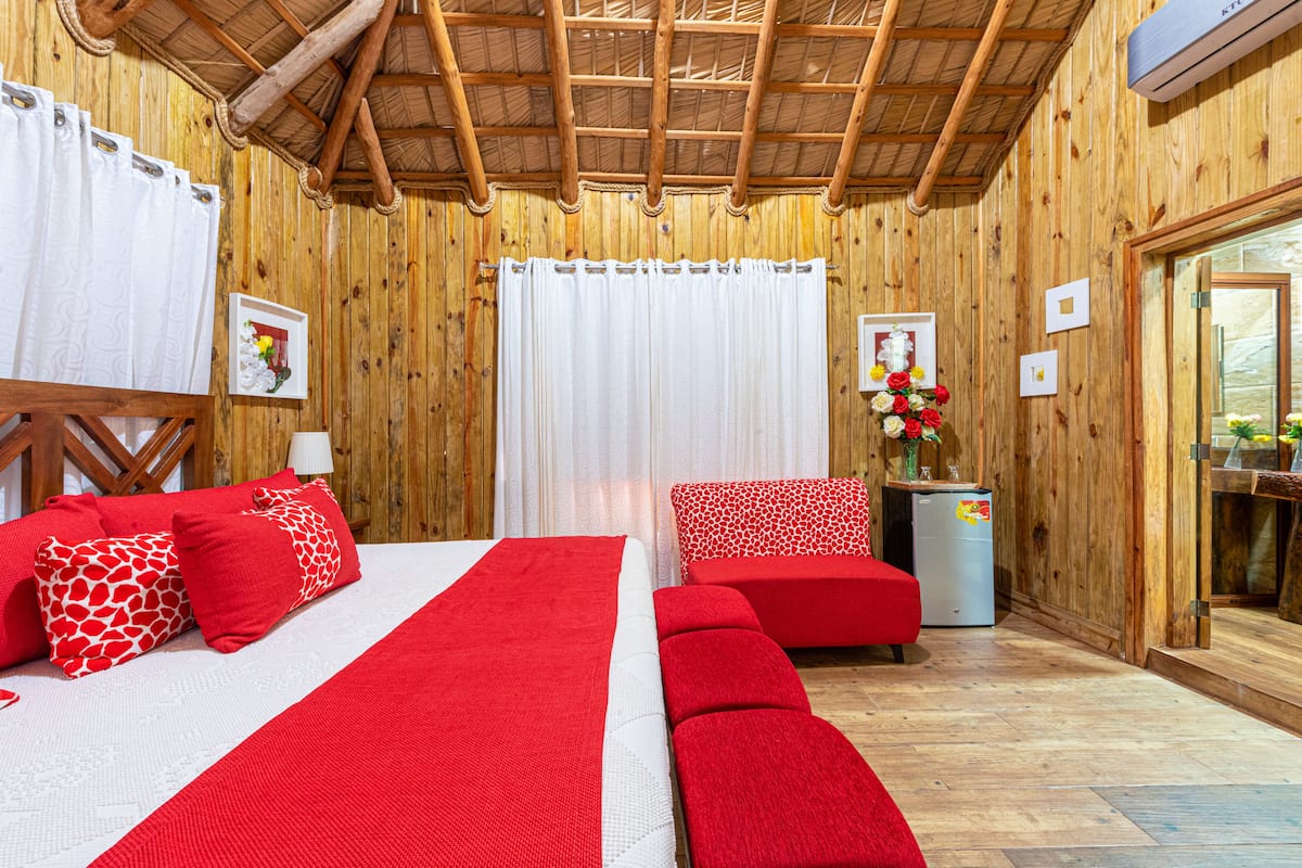 A wooden room with a bed, a sofa, and a small table with flowers.