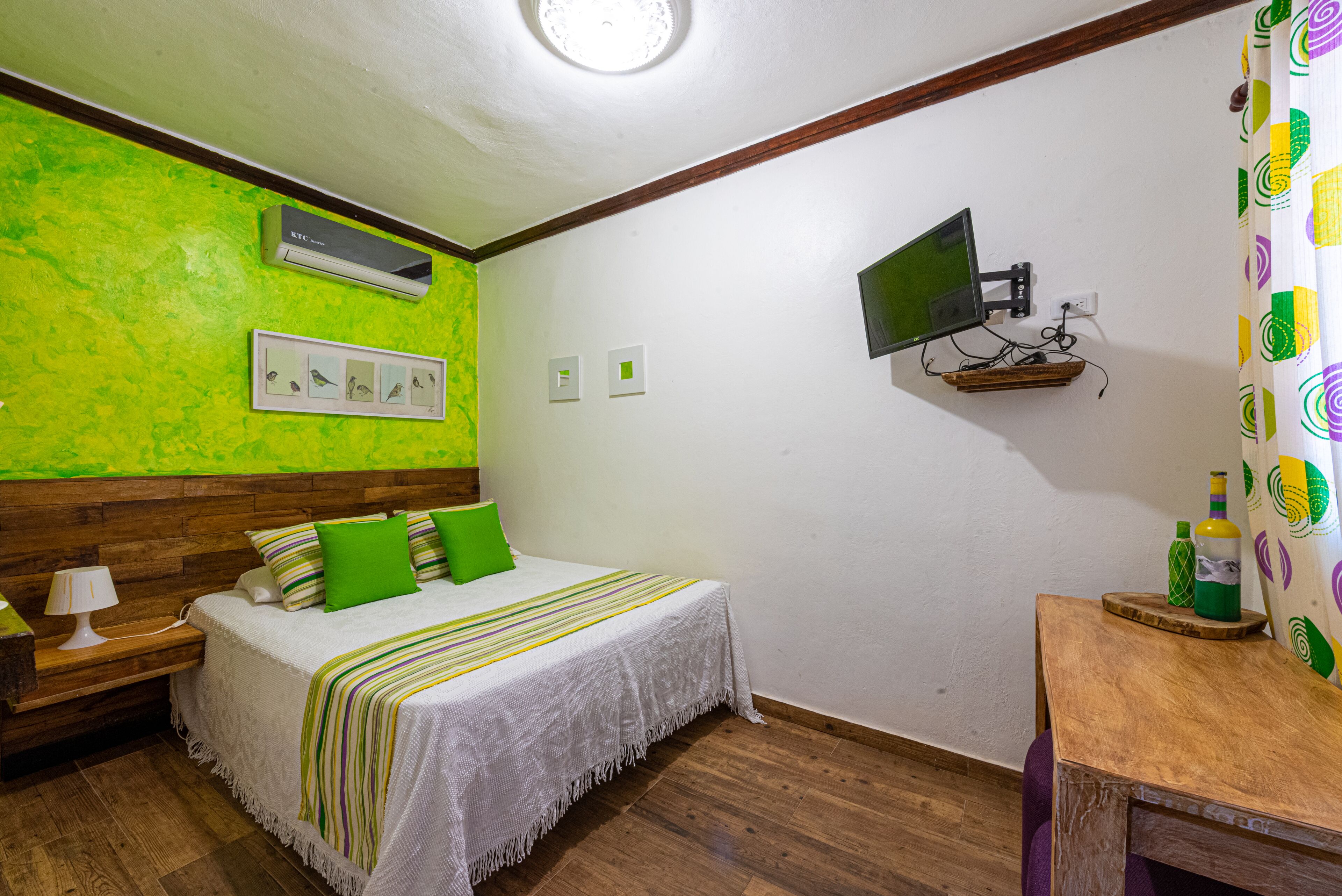 A bedroom with a bed, a bedside table, a TV mounted on the wall, and an air conditioner.