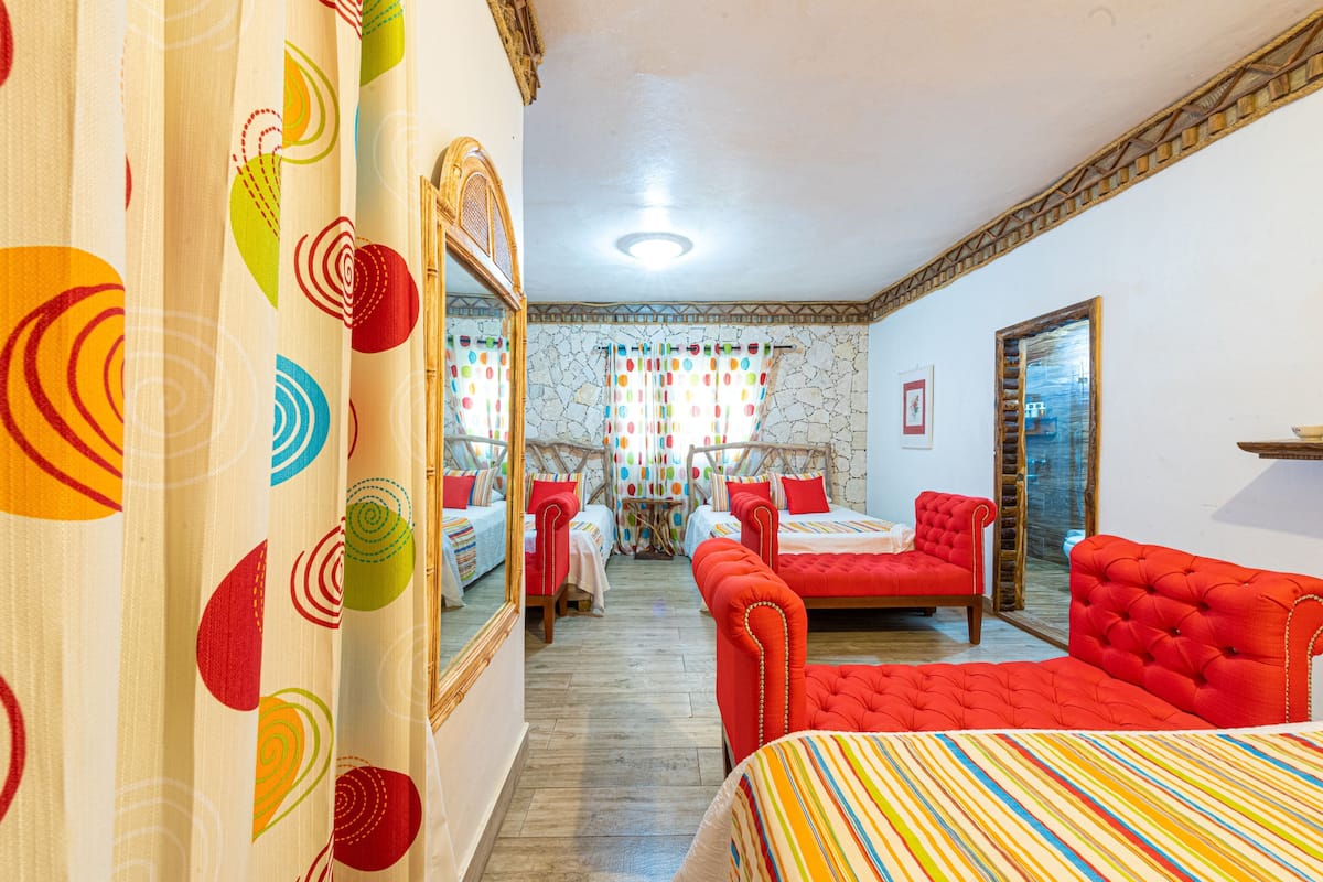 A hotel room with a bed, a sofa, a mirror, and a view of the street through a window.