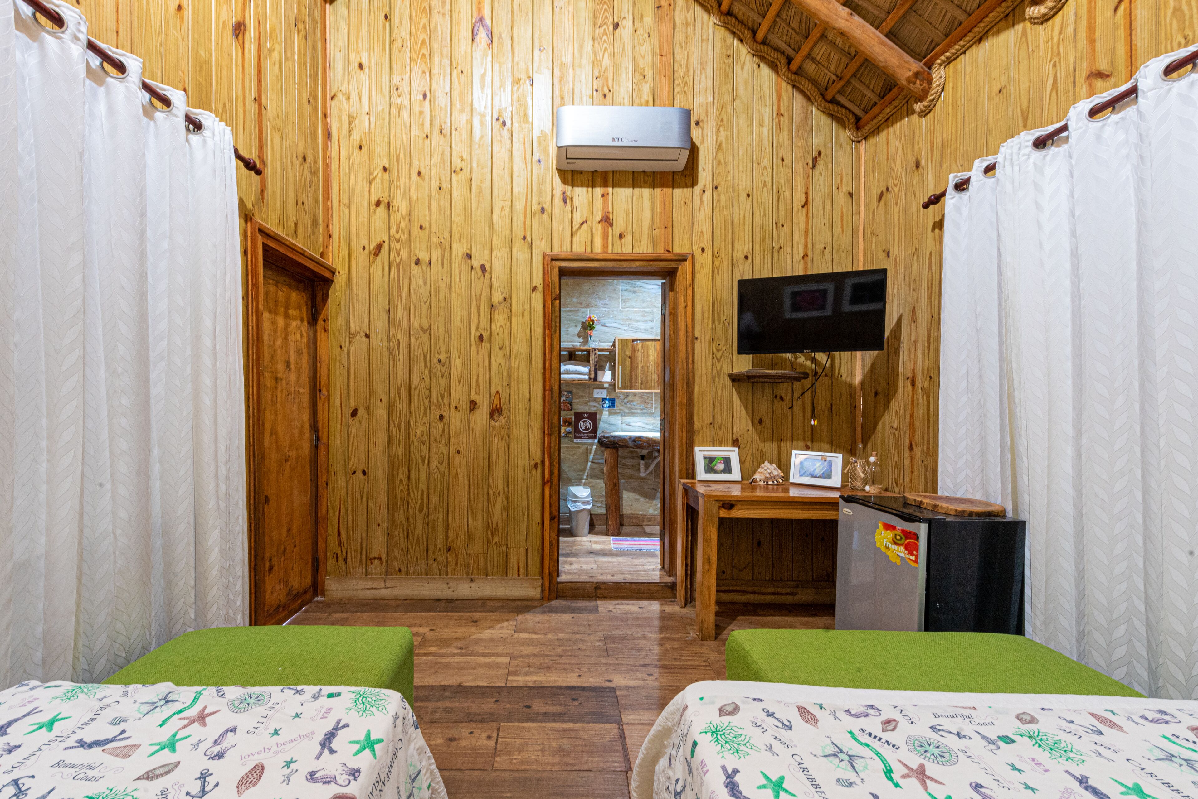 A wooden room with two beds, a TV, and a kitchenette.