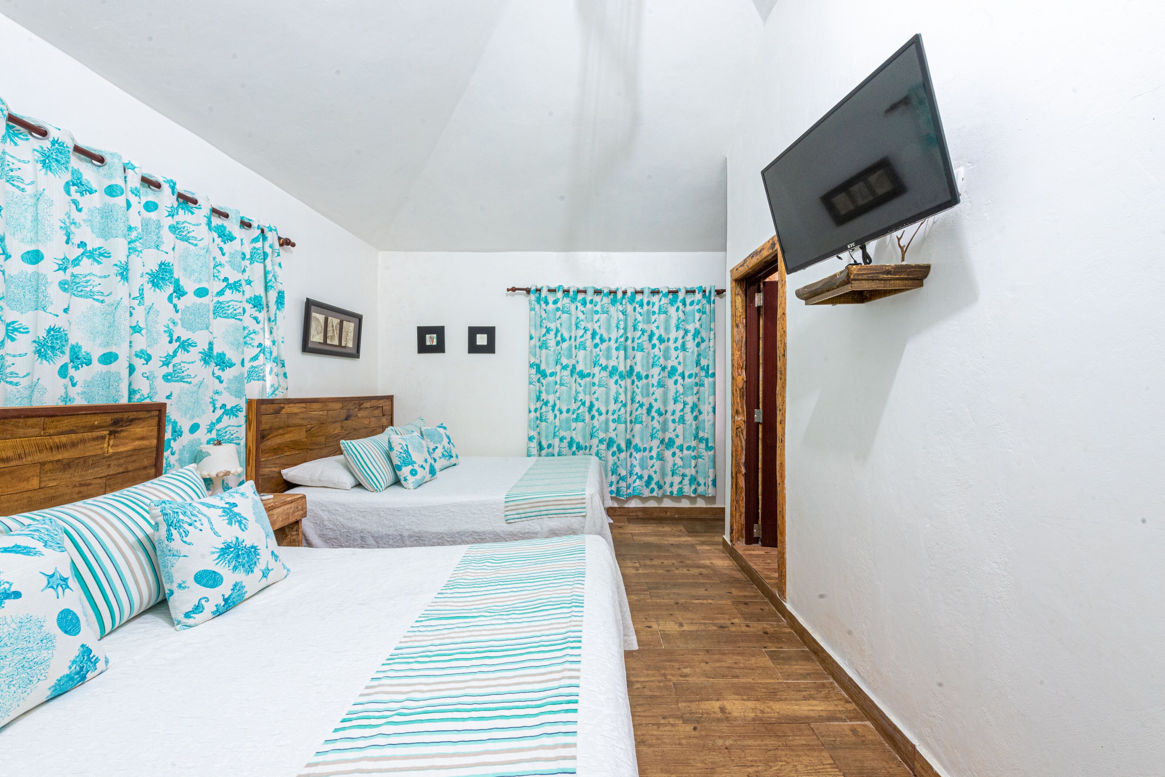A bedroom with two beds, a TV mounted on the wall, and a wooden floor.