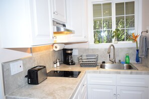 A modern kitchen with white cabinets, a built-in stove, a coffee maker, and a window with a view of greenery.