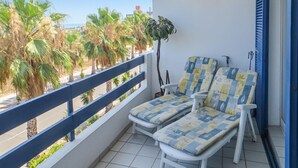 A balcony with two white lounge chairs, a potted plant, and a view of palm trees and buildings. - 2 bedroom lovely apartment in Orihuela costa (Orihuela costa)