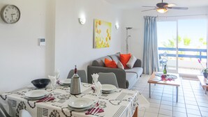 A dining area with a table set for two, a sofa with cushions, a ceiling fan, and a view of the outdoors. - 2 bedroom lovely apartment in Orihuela costa (Orihuela costa)