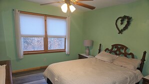 A bedroom with a bed, a nightstand, a lamp, a ceiling fan, a window with curtains, and a wall decoration. - 3 Bedroom home with rear deck and covered front porch. (Delancey)