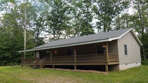 A single-story cabin with a porch, surrounded by trees. - 3 Bedroom home with rear deck and covered front porch. (Delancey)