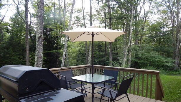 A deck with a grill, table, chairs, and an umbrella. - 3 Bedroom home with rear deck and covered front porch. (Delancey)