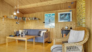 Une pièce chaleureuse avec un décor intérieur en bois, un canapé, un fauteuil en osier, une table avec des bougies et des étagères à livres.