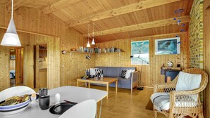 L’intérieur est en bois et comprend une table à manger, un canapé et un fauteuil en osier. On y trouve également des étagères à livres et des tableaux accrochés aux murs.