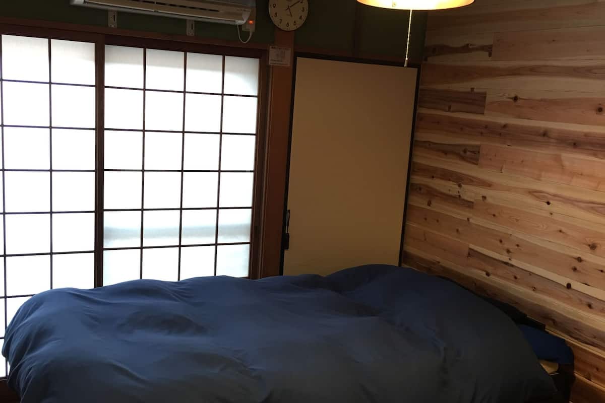 A room with a bed, a clock, an air conditioner, and a view through a shoji screen.