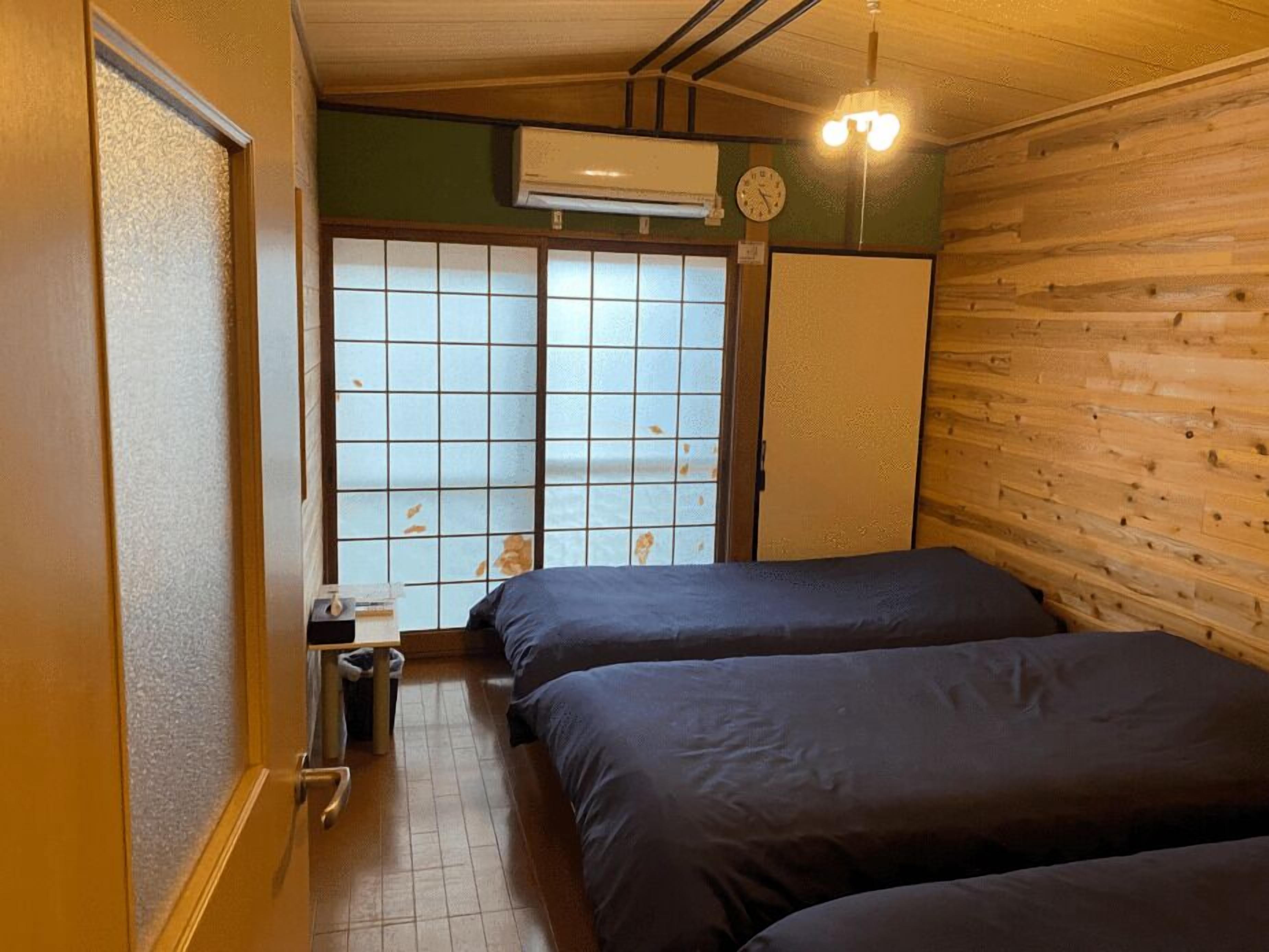 Une chambre avec deux lits, un mur en bois, une fenêtre à croisillons et un climatiseur fixé au mur.