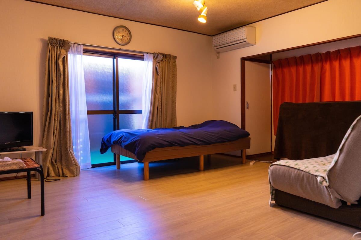 A room with a bed, a TV, a sofa, and a window with curtains.
