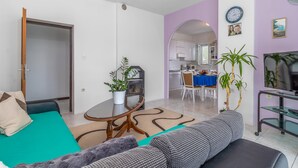 Ein modernes Wohnzimmer mit einer Couch, einem Couchtisch und einem Essbereich mit blauer Tischdecke.
