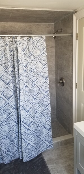 A shower area with a patterned curtain, a showerhead, and a door leading to a bathroom. - Newly renovated cottage (Point Pleasant Beach)
