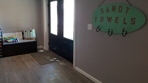 Ein Flur mit einer schwarzen Tür, einem an der Wand befestigten Schild mit der Aufschrift "SANDY TOWELS" und einer Bank mit gefalteter Kleidung.