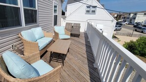 Eine überdachte Terrasse im Freien mit Korbmöbeln und einem Tisch, mit Blick auf eine Straße mit geparkten Autos.
