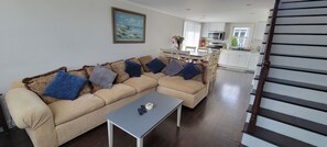 A living room with a beige sectional sofa, a coffee table, and a kitchen in the background. - Newly renovated cottage (Point Pleasant Beach)