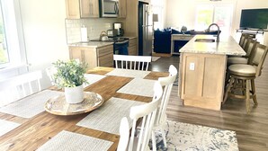 Une cuisine moderne avec des meubles en bois, un îlot central et un coin repas comprenant une table en bois et des chaises blanches.
