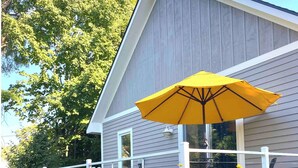 Une maison avec un porche couvert, un parasol jaune et des fleurs jaunes au premier plan.