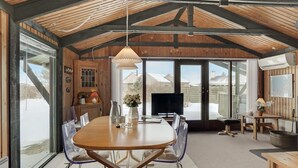 A spacious dining area with a wooden table and chairs, a television, and a large window offering a view of a snowy landscape.