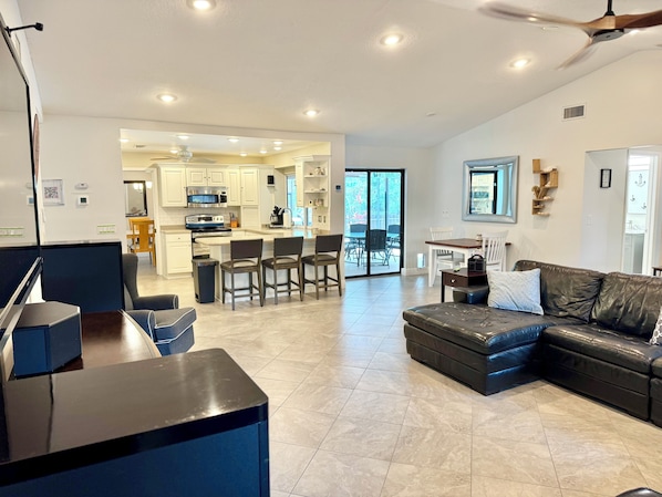 A modern living room with a leather sofa, a dining area, and a kitchen with white cabinets.