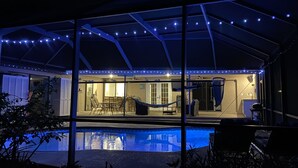 Un espace extérieur abrité comprenant une piscine, des sièges et des guirlandes lumineuses.