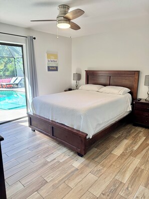A bedroom with a wooden bed, a ceiling fan, and a view of a swimming pool through a glass door. - Family Friendly heated pool Home 2000sqft <br>“NO parties” (Palm Harbor)