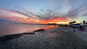 Une plage au coucher du soleil, avec une mer calme, un rivage sablonneux et des voitures garées.
