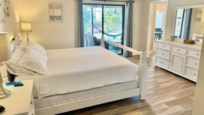Une chambre à coucher comprenant un lit, des lampes de chevet, une commode, un ventilateur de plafond et une vue sur l’extérieur grâce à une porte coulissante.