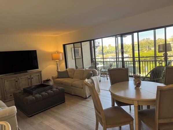 A spacious living area with a flat-screen TV, a sofa, a coffee table, and a dining table with chairs.
