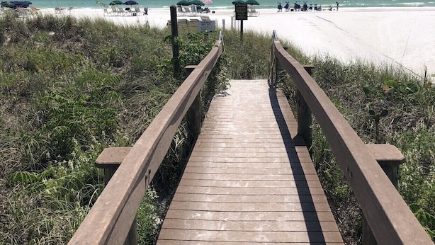 Een houten looppad dat naar een strand leidt, met parasols en ligstoelen.