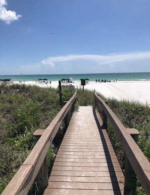A wooden boardwalk leading to a beach with umbrellas and lounge chairs.