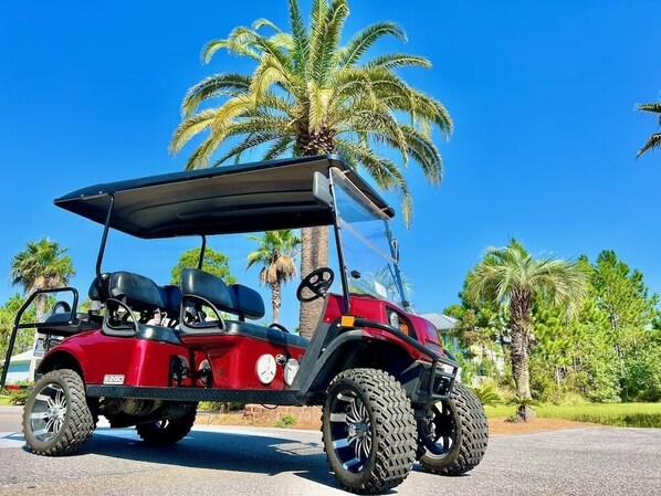 Une voiturette de golf rouge est garée sur une surface pavée, avec des palmiers en arrière-plan.
