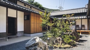 Un edificio japonés tradicional con fachada de madera, tejado de tejas y un patio de grava con rocas y plantas.