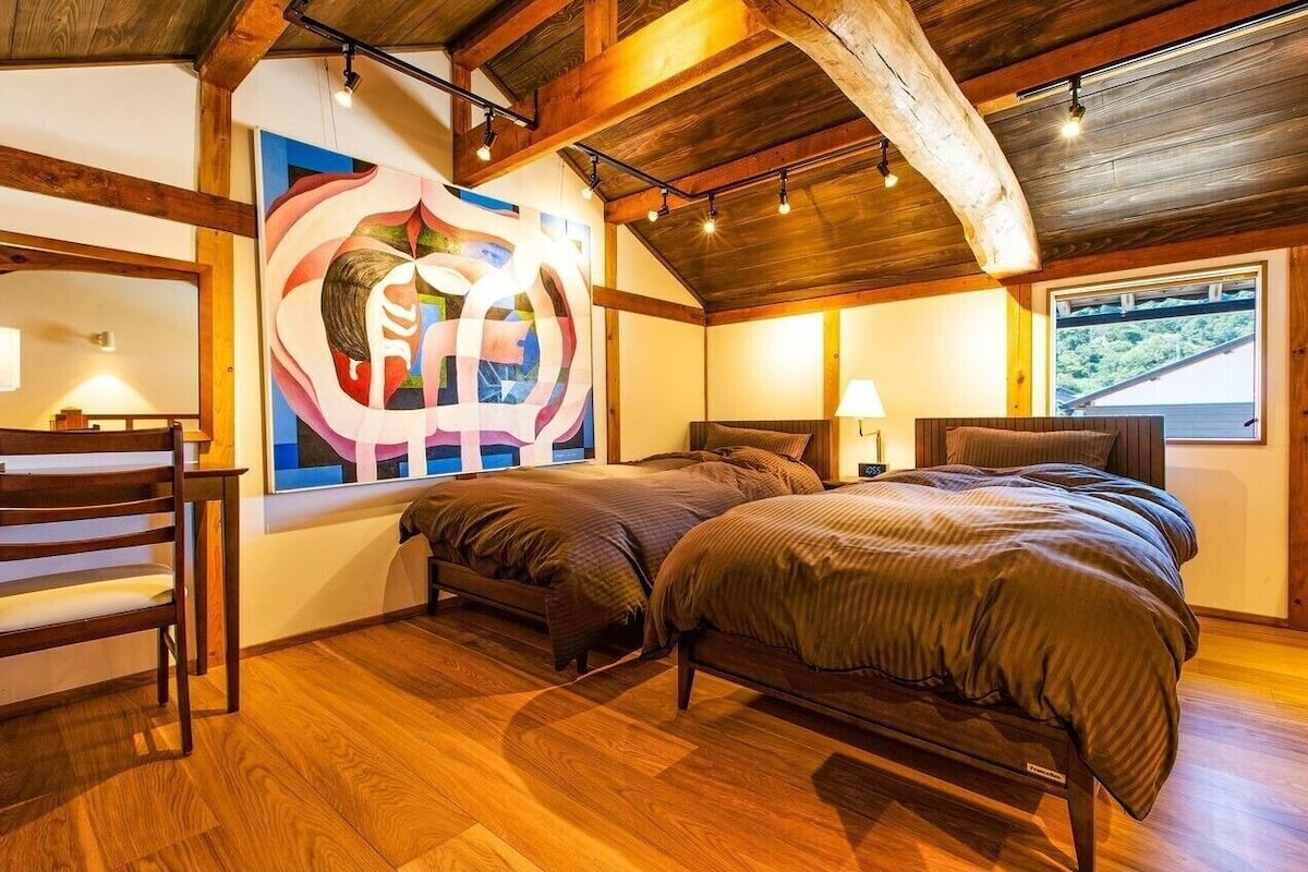 Un dormitorio con dos camas, suelo de madera, un ventanal grande y un cuadro en la pared.