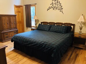 Une chambre à coucher avec un lit en bois, une table de chevet avec une lampe, une commode et une fenêtre avec des rideaux.