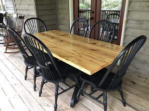 Une table de salle à manger en bois, entourée de chaises noires, sur une terrasse en bois.