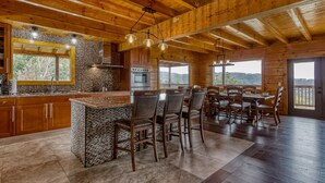 Una cocina amplia con encimeras de granito, armarios de madera y una isla grande con taburetes de bar. Varias ventanas ofrecen vistas del paisaje circundante.
