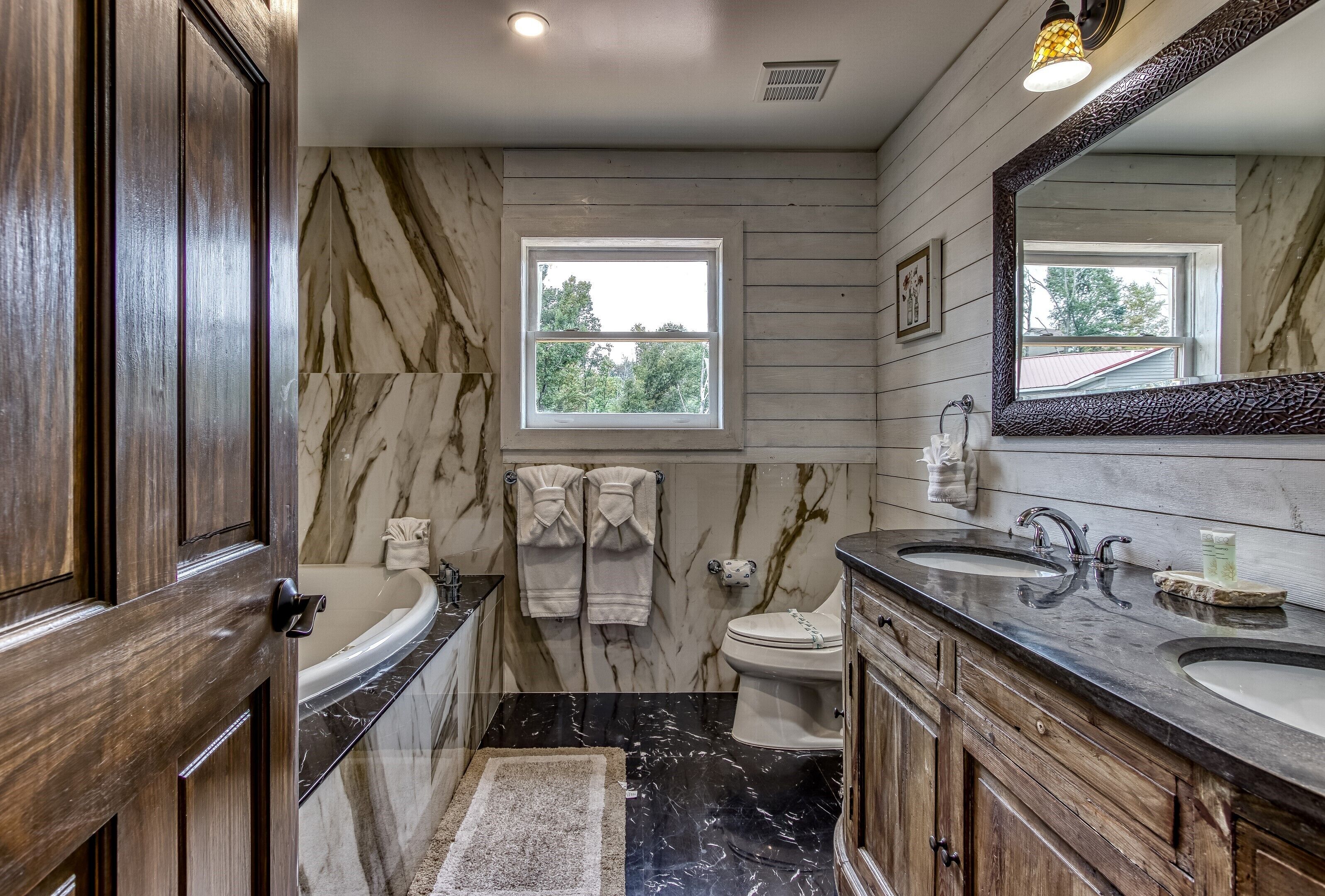 A bathroom with a marble vanity, dual sinks, a toilet, and a window.