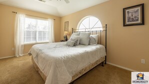 A bedroom with a bed, a ceiling fan, a window with blinds, a lamp, and a framed picture on the wall.