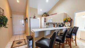 A compact kitchen with a white refrigerator, a microwave, and a coffee machine. There are four black chairs around a small dining table.