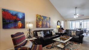 A living room with a black leather sofa, a patterned armchair, a coffee table, and two paintings on the wall.