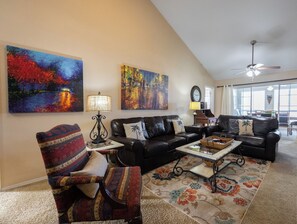 A living room with a black leather sofa, a patterned armchair, a coffee table, and two paintings on the wall.
