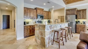 A spacious kitchen with wooden cabinets, a stone island, and a modern refrigerator.