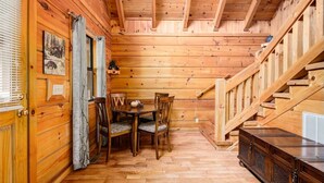 A wooden cabin interior with a dining area, a staircase, and a small cabinet.